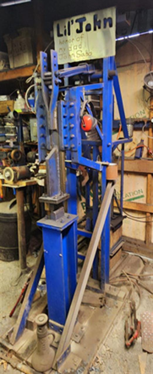 The blue I beam and channel iron frame holds a vertical cylinder used for pounding metal.